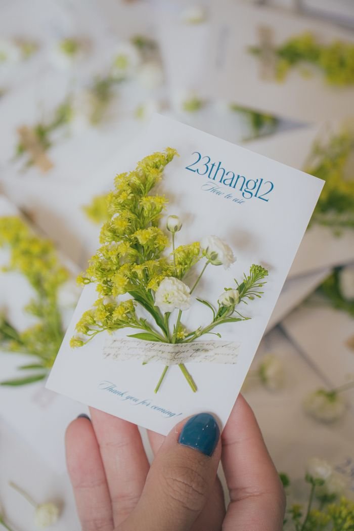team-01 Hand holds a floral invitation card with vibrant yellow and white flowers.