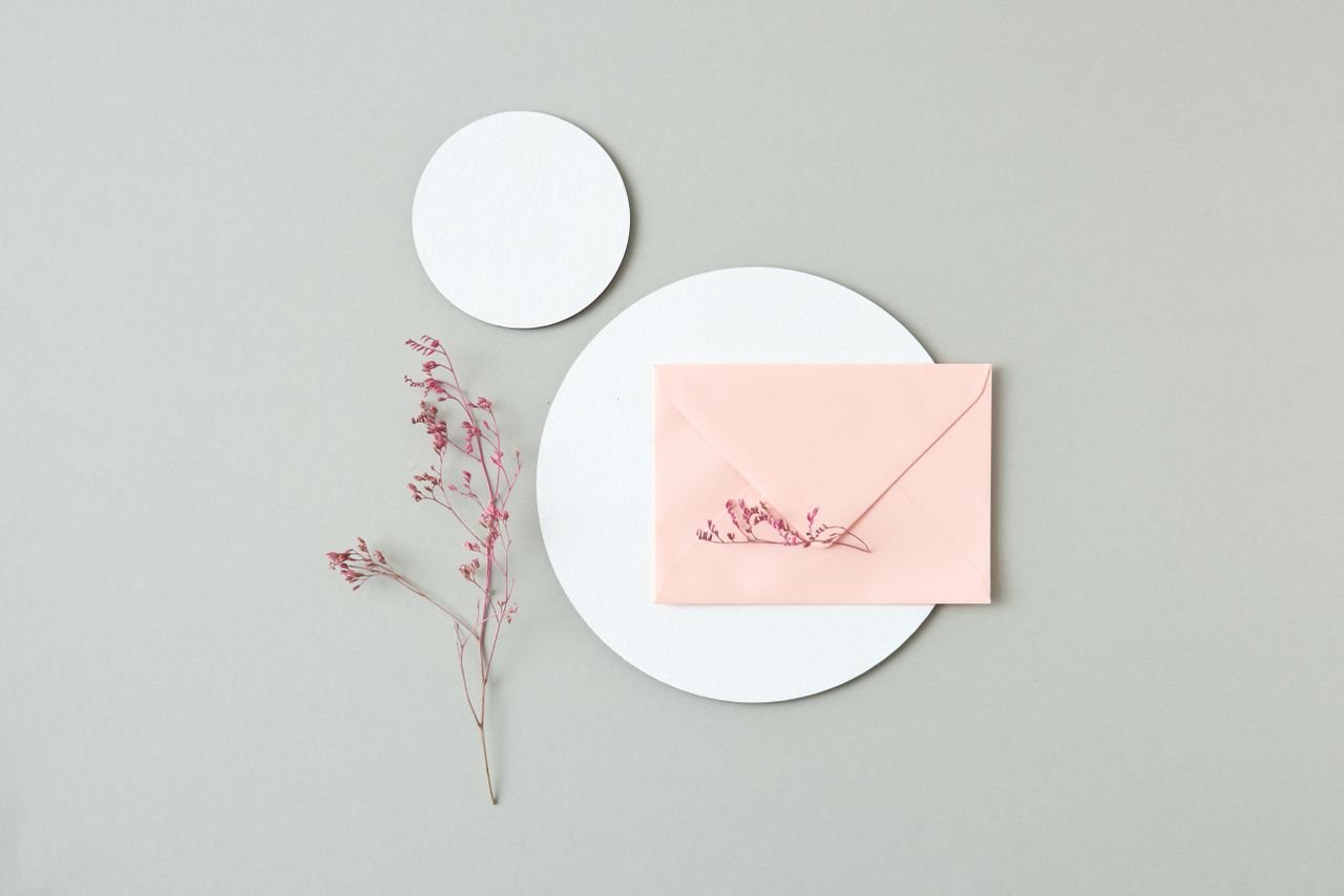 Top view of a pink envelope with floral accents on a minimalist background.